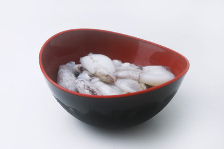 Raw and fresh squid is in a black bowl on an isolated white background.