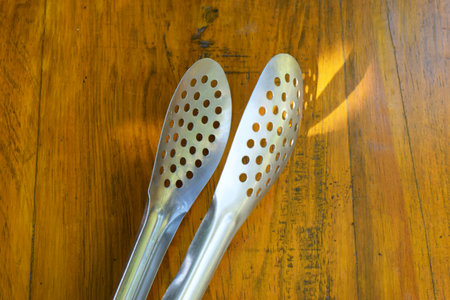 A silver kitchen cooking tongs sits on a wooden table and a green garden backgroundの写真素材
