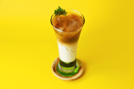 Pandan iced coffee drink layered with melon syrup, milk and chocolate coffee in a tall glass on a yellow backgroundの写真素材