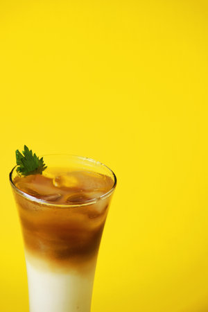 Closeup photo of a pandan iced coffee drink layered with melon syrup, milk and chocolate coffee in a tall glass on a yellow backgroundの写真素材