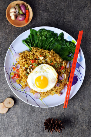 Fried noodles with sunny side up egg and mixed vegetables on a plate with a cement backgroundの写真素材