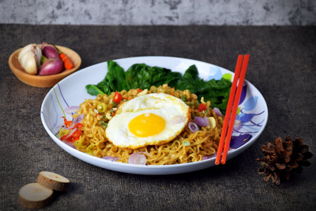 Fried noodles with sunny side up egg and mixed vegetables on a plate with a cement backgroundの写真素材