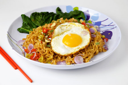 Fried noodles with sunny side up egg and mixed vegetables on a plate with an isolated white backgroundの写真素材