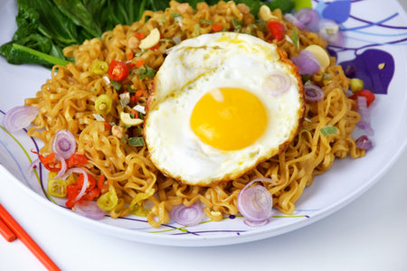 Closeup photo of Fried noodles with sunny side up egg and mixed vegetables on a plate on an isolated white backgroundの写真素材