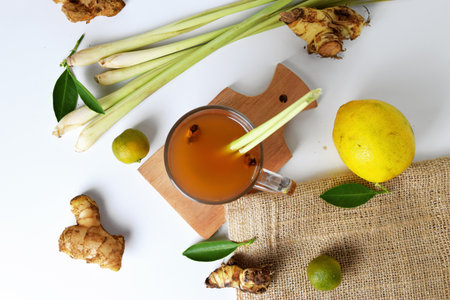 Top view photo of Hot red ginger drink in a glass cup with some raw ginger, lemon, squeezed orange, spring onion and white isolated background. Healthy drinks can be used for treatmentの写真素材