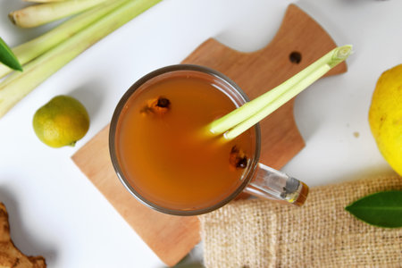 Top view photo of Hot red ginger drink in a glass cup with some raw ginger, lemon, squeezed orange, spring onion and white isolated background. Healthy drinksの写真素材