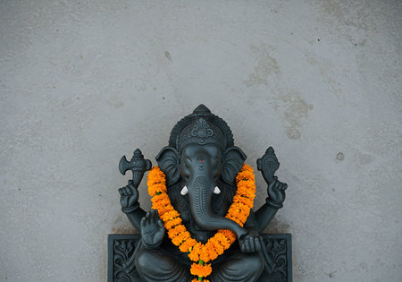 Close-up of a dark gray or black statue of Ganesha, the Hindu god of beginnings, prominently displayed against a light gray, textured wall. Generative Aiの素材