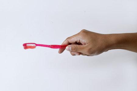 Male hand holding a red and white toothbrush containing toothpaste on a white isolated backgroundの写真素材