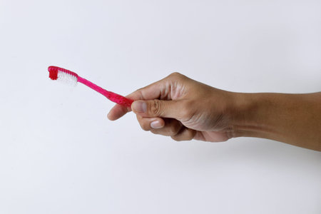 Male hand holding a red and white toothbrush containing toothpaste on a white isolated background