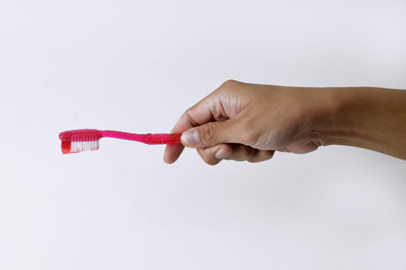 Male hand holding a red and white toothbrush containing toothpaste on a white isolated background