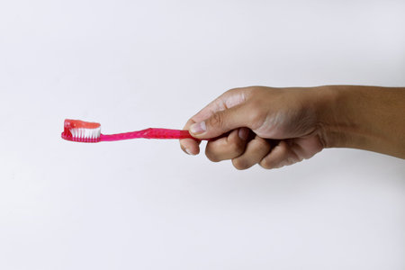 Male hand holding a red and white toothbrush containing toothpaste on a white isolated background