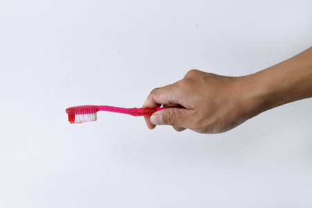 Male hand holding a red and white toothbrush containing toothpaste on a white isolated background