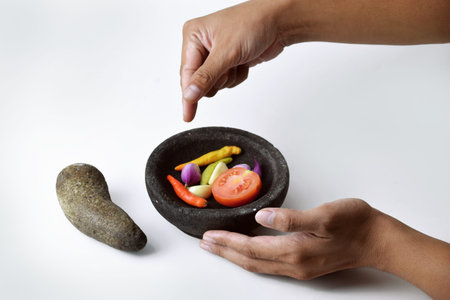 A man shows the ingredients for making chili sauce using cayenne pepper, onions and tomatoes in a...