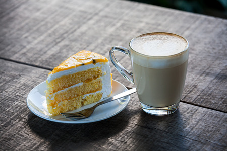 Yellow cake with cup of latte coffee on old wood tableの写真素材