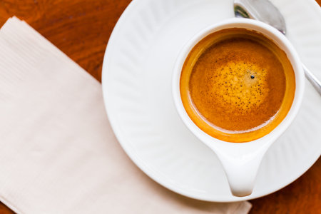 Cup of fresh espresso with spoon, napkin on table, view from above