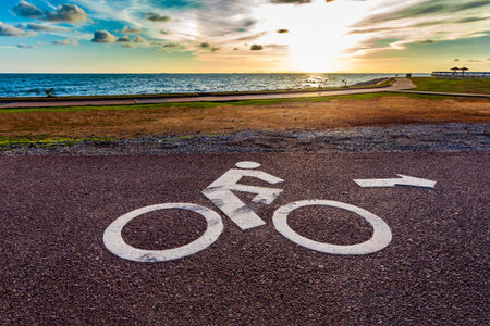 White bicycle road sign on asphalt lane and seascape in sunset