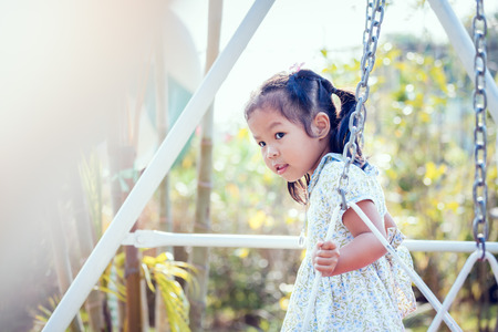 Asia little girl is playing swing at backyard in sunny dayの写真素材