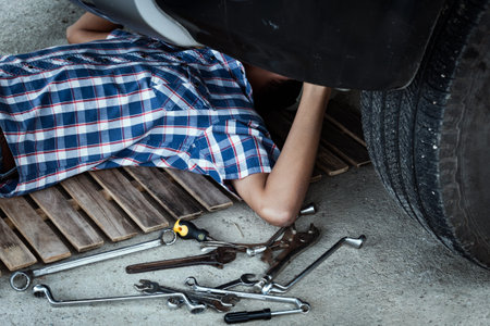 Mechanic lying down and working under the front of automobile in store, day timeの写真素材