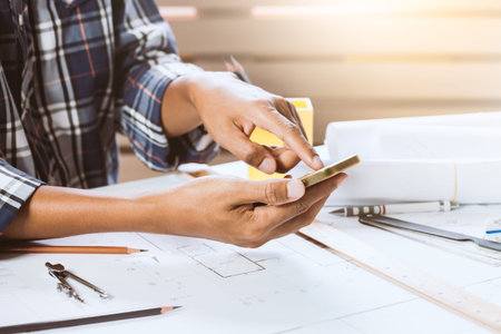 Close-up of engineer male using phone in workspace. Concept of builder working on house project.の写真素材