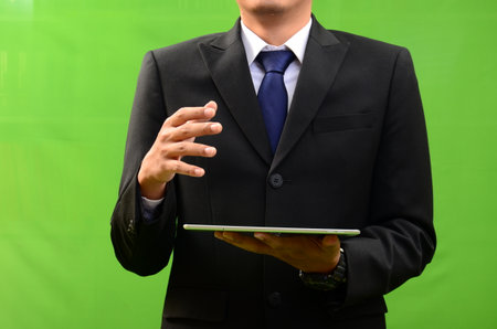 Businessman holding digital tablet on green background. Business and technology conceptの写真素材
