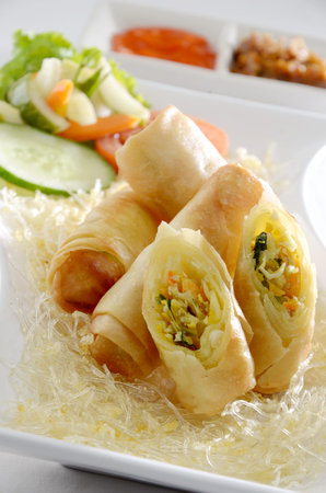 Fried spring rolls with vegetables and sweet sauce on white plate.