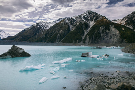 A glacial lake filled with icebergs, set against rugged mountains, with the dynamic interplay of...