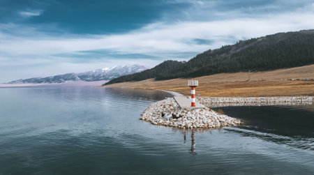 Aerial panoramic view of a lake with a lighthouse and mountains in the backgroundの写真素材