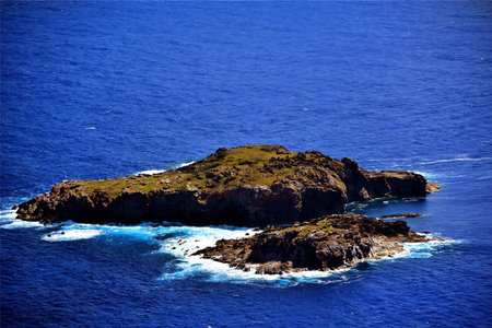 An isolated rock islet rises from the deep blue sea, its rugged beauty highlighted by the white foam...