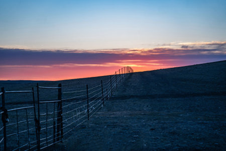 A wire fence extends towards the horizon, leading to a stunning sunset.の写真素材
