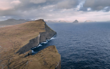 Stunning aerial view of rugged cliffs meeting the ocean in the Faroe Islands under a cloudy sky. A remote and scenic landscape.の写真素材