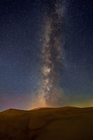 Stunning view of the Milky Way galaxy stretching over the vast desert dunes at night, creating a breathtaking celestial landscape.の写真素材