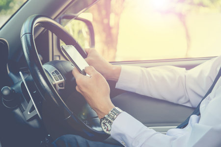 Businessman touching and using smartphone for online chat In front of steering wheel at Front seat...