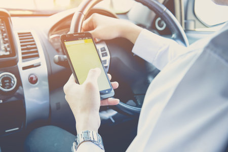Businessman touching and using smartphone for online chat In front of steering wheel at Front seat...