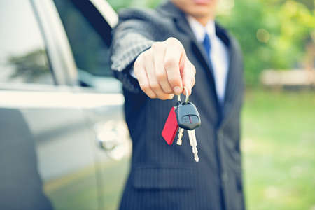 Male holding car keys with car on background,car keys, seller hand giving keys, dealership and sales conceptの写真素材