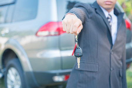 Male holding car keys with car on background,car keys, seller hand giving keys, dealership and sales conceptの写真素材