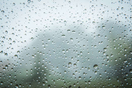Rain drops on window glasses surface with cloudy background , natural pattern of raindrops isolated on cloudy background.の写真素材
