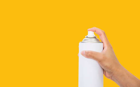 hand holds a spray of white paint on yellow background.の写真素材