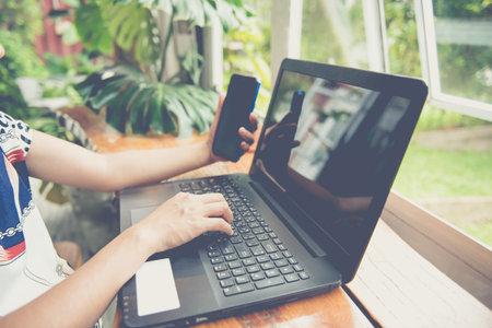 female holding smartphone getting message with confirmation making transaction on laptop...