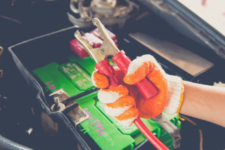 Mechanic hand charging battery of a car with electricity through jumper cables.Maintenance and repair.の写真素材