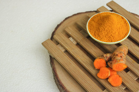 Turmeric powder in a bowl and fresh turmeric root on wooden backgroundの写真素材
