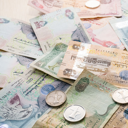 Closeup of different UAE dirhams currency notes and coins, paper money on a light wooden table from high angleの写真素材