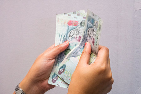 Closeup of a female's hands counting UAE 500 dirhams currency notes, paper money against a light backgroundの写真素材