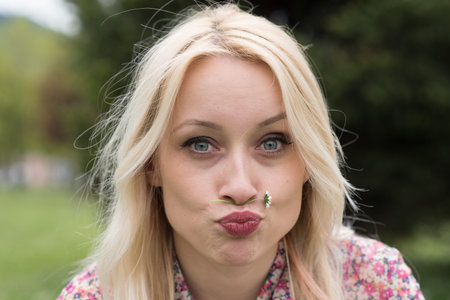 blond girl with flower between nose and mouth