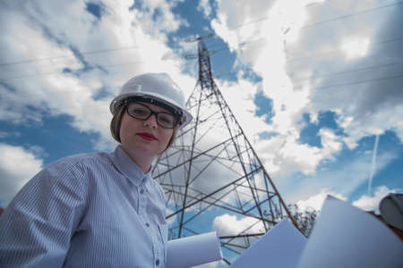 woman engineer standing  at power lines and holding blueprintsの写真素材