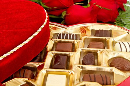 A box of assorted chocolate candies with red roses around themの写真素材