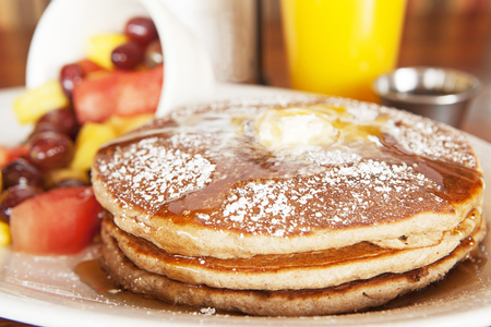 Stack of three golden pancakes with butter, syrup and powdered sugar served with fresh fruit and orange juiceの写真素材
