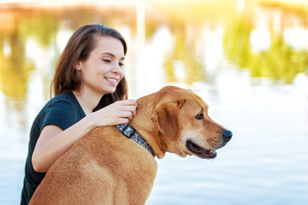 Happy girl and her Labrador crossbreed dog looking out over a lake