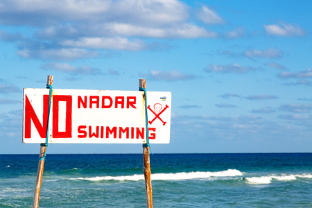 Danger no swimming sign with skull and crossbones posted on a beach with rough surf on the Caribbean Seaの写真素材
