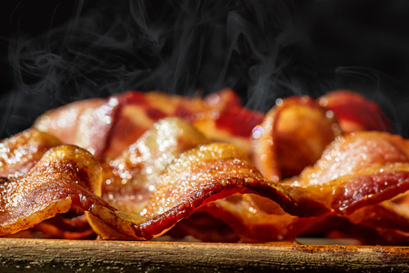 Closeup photo of a pile of freshly cooked hot crispy bacon resting on a wood cutting boardの写真素材