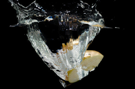Apple slice falling into splashing water, isolated on black background.の写真素材